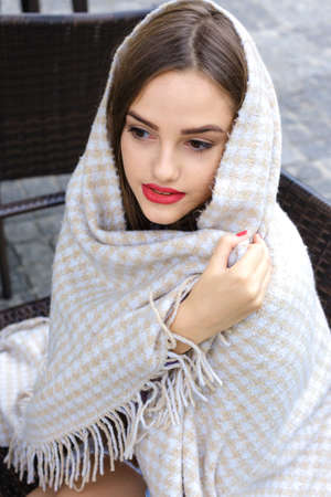 beautiful girl wrapped in a blanket sitting in a outdoor cafeの写真素材