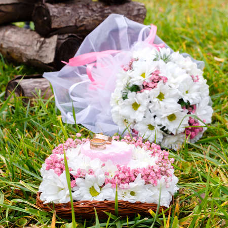 Wedding rings on a stand and a bridal bouquet of white chamomiles on a green grass. Selective focus.の写真素材
