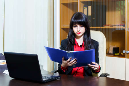 Attractive businesswoman sitting at workplace in the office, intently reading the documents