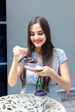 Beautiful young girl eating a cake in outdoors cafe at summer day.
