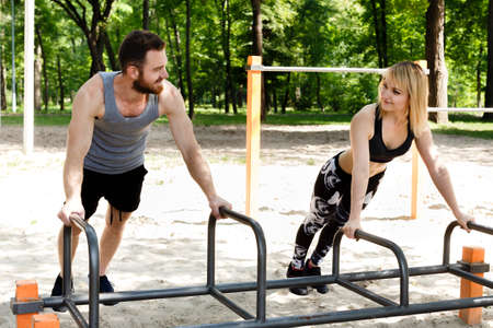 Young sportive woman and bearded man doing push-ups exercises in a parrk at summer day.の写真素材