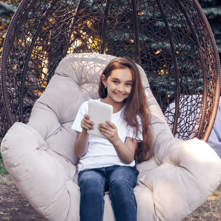 Smiling caucasian girl holding white  tablet PC, sitting in a park at summer day. Looking at camera.の写真素材