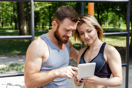 Young caucasian blonde girl and bearded man browsing the internet on a white tablet PC while doing...