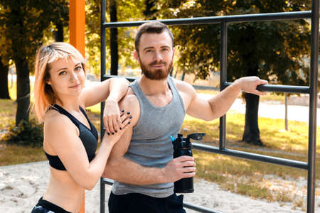 Sporty blonde girl and bearded man is resting after workout training in a park at autumn day. Man...