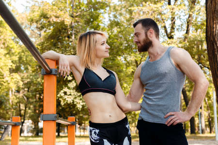 Young athletic girl and bearded man talking while relaxing on training in the park at autumn day.の写真素材
