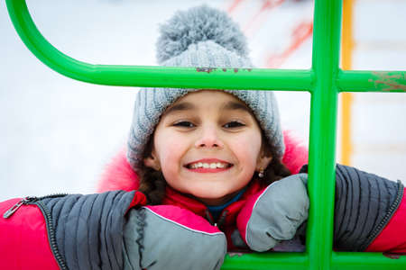 Happy girl playing on a  playground in a city park at winter frosty day.