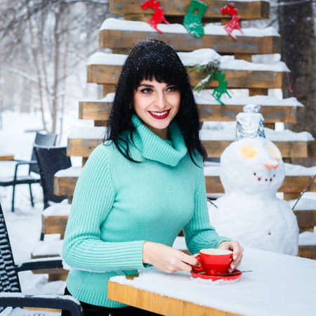 Attractive young woman drinks a coffe in street cafe at snowy winter day.の写真素材