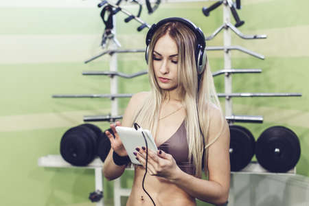 Beautiful young blond woman browsing the Internet using a tablet PC, training in a gym.