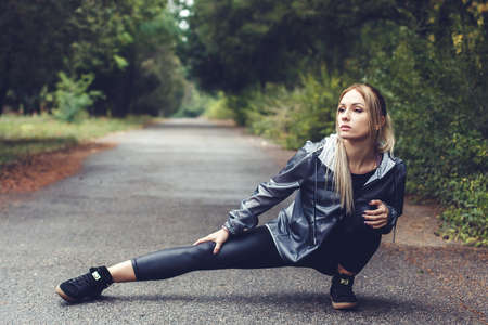 beautiful young woman doing stretching exercises, training in a city park at rainy weather. Healthy lifestyle concept.の写真素材