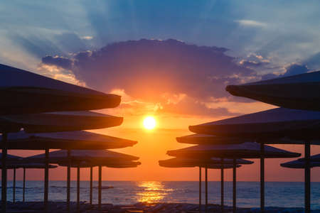 Silhuettes of beach umbrellas on a deserted beach in the evening on a sunset backgroundの写真素材