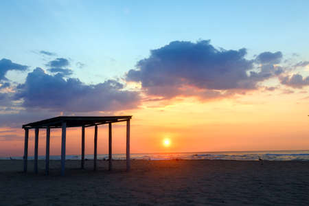 Silhouette gazebo on an empty sandy beach on a sunset background.の写真素材