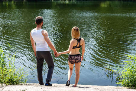young couple walking in the park near the river at sunny summer day.