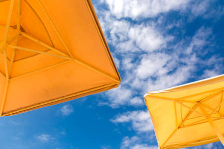 Beach umbrellas on a blue cloudy sky background, bottom view. Travel, beach relax concept.の写真素材