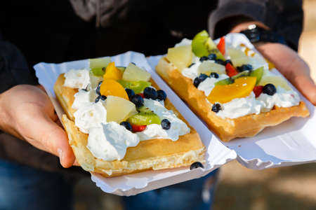 Man holding two fresh waffle cakes with fruit and whipped cream on a holiday.の写真素材