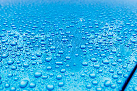 Rain drops close-up on a turquoise car body with Hydrophobic Effect.