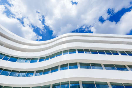 Curved Glass Exterior Of Modern Office Building on a Blue Cloudy Sky Background.のeditorial素材