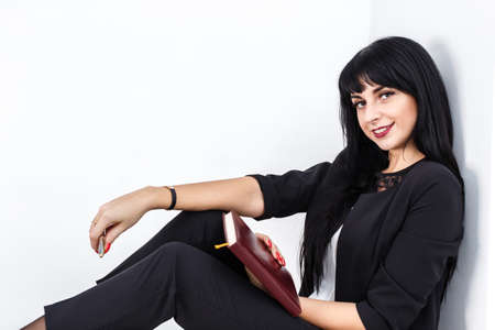 Young Beautiful happy brunette woman holding a notebook dressed in a black business suit sitting on...