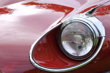 Headlight and hood of old retro red racing car ckose-up.