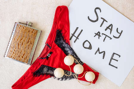 Women's red bikini panties, metal flask with alcoholic drink, sign Stay home, and sex toy of four...