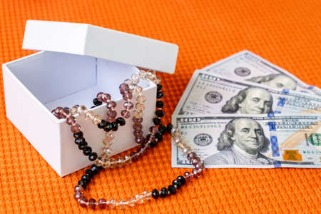 Beautiful Female Beads in White Gift Box and US Paper currency Dollars Lay on a Orange Fabric Textured Background.の写真素材