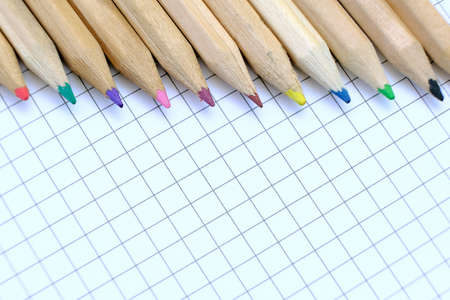 Closeup set of  multicolored pencils on the checkered paper sheet of notebook for the drawing. Back...