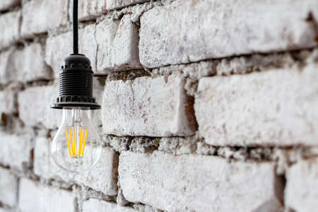 Energy saving LED lamp hanging on a background of a rough white wall in a luxury design of modern loft hotel room.の写真素材