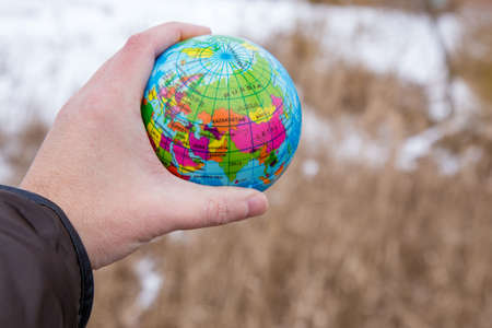Male Hand Holding a Globe of Planet Earth on a snow Background at cold Winter Day.の写真素材