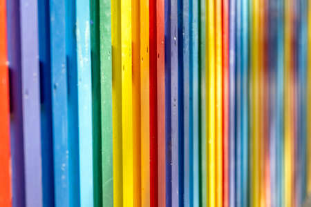 Part of wooden, rainbow colorful painted fence  on a sunny hot summer day in a city park. Abstract multicolored background.の写真素材