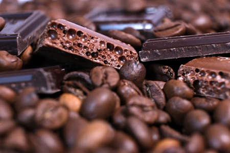 Close-up of dark roasted coffee beans and chocolate background. Aromatic coffee grains and sweet...