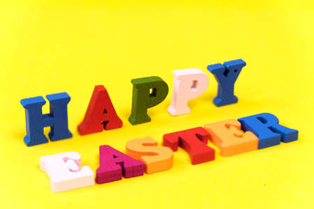 Words Happy Easter of colorful toy alphabet letters isolated on yellow background. Ideal for design of bright greeting card. Shallow depth of field.の写真素材
