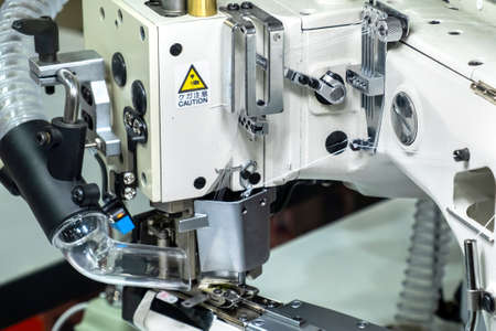 Close-up of details of modern white professional electric sewing machine on a table in factory. Work...