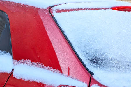 Close-up of snow covered red car under blizzard. Cold winter frosty snowy background.の写真素材
