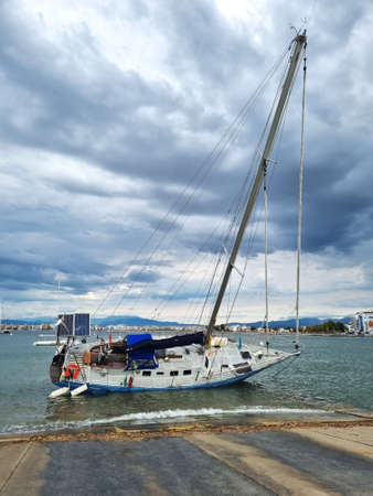 Overturned yacht stranded on the shore of the sea beach on a cloudy day. Consequences of a storm in...