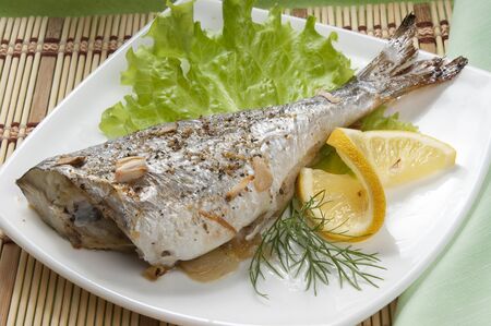 Baked sea bream with lettuce and lemon on the white plateの写真素材