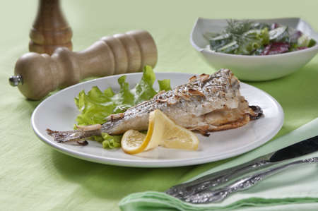 Baked sea bream with lettuce, lemon and parsley on the white plate