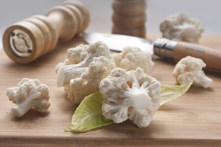 Pieces of cauliflower on the wooden board with knife and pepper millの写真素材