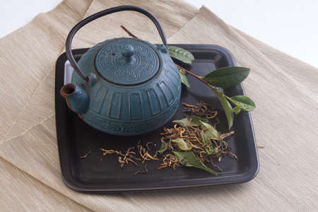 Black plate with blue teapot, green tea branch and dried tea leaves on the napkinの写真素材