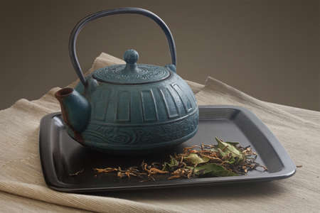 Black plate with blue teapot and green dried tea on the napkinの写真素材