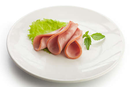 Three rolled pieces of ham with fresh green basil on the white plateの写真素材