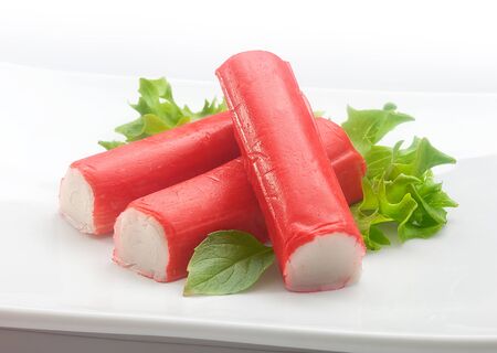 Three red crab stick with green basil and lettuce on the white plateの写真素材