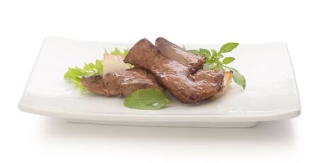 Fried pieces of beef liver with fresh green lettuce, basil and fried onion on the white plateの写真素材
