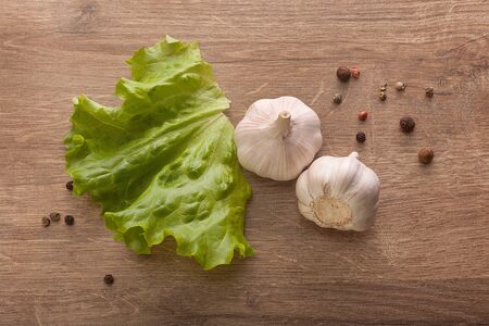 Top view of two head of garlic, fresh green lettuce and black pepper on the wooden tableの写真素材