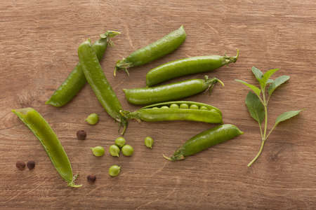 Top view of fresh green pea pods and branch of basil on the wooden table