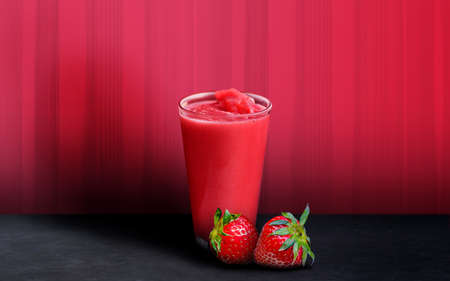 strawbery juice in a glass with two straberry fruits on red backgroundの写真素材