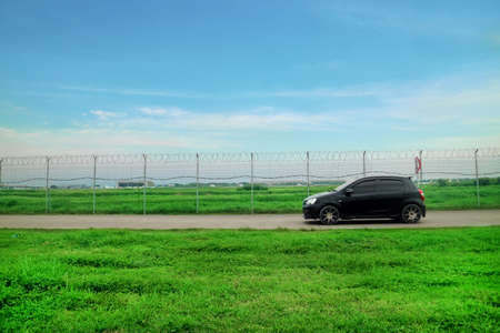 Road Outside Airport Lined by a Wire Fence with green grass and black carの写真素材