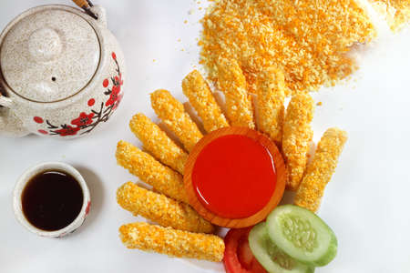 Food photography of Nugget sticks fish fried crunchy line up around with ketchup cucumber tomatoes on white tray with breaded sprinkles teapot and cup white background top viewの写真素材