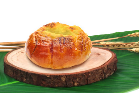 Freshly Baked Golden Custard Bun on Wooden Board with Green Leaf Background
