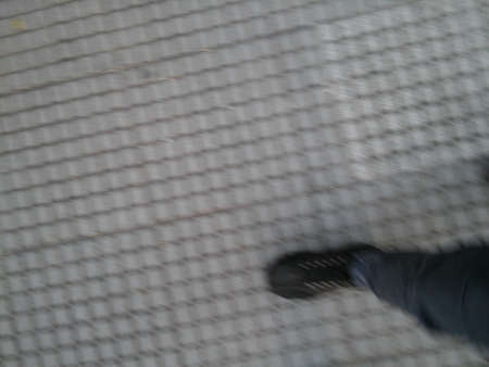 Background of feet with black shoes walking of a sidewalk with different elements in daylight