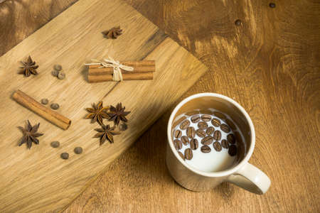 A cup of milk and coffee beans on the serving wooden board star anise, cinnamon and allspice.の写真素材