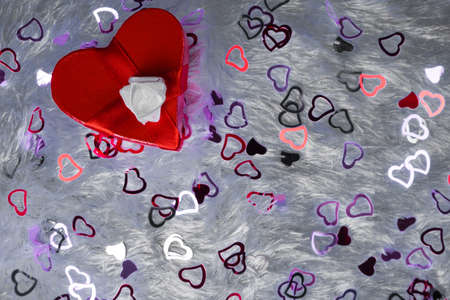 Gift box in the shape of a heart and tied with a red ribbon with a bow in the shape of a rose on a pillow.の写真素材